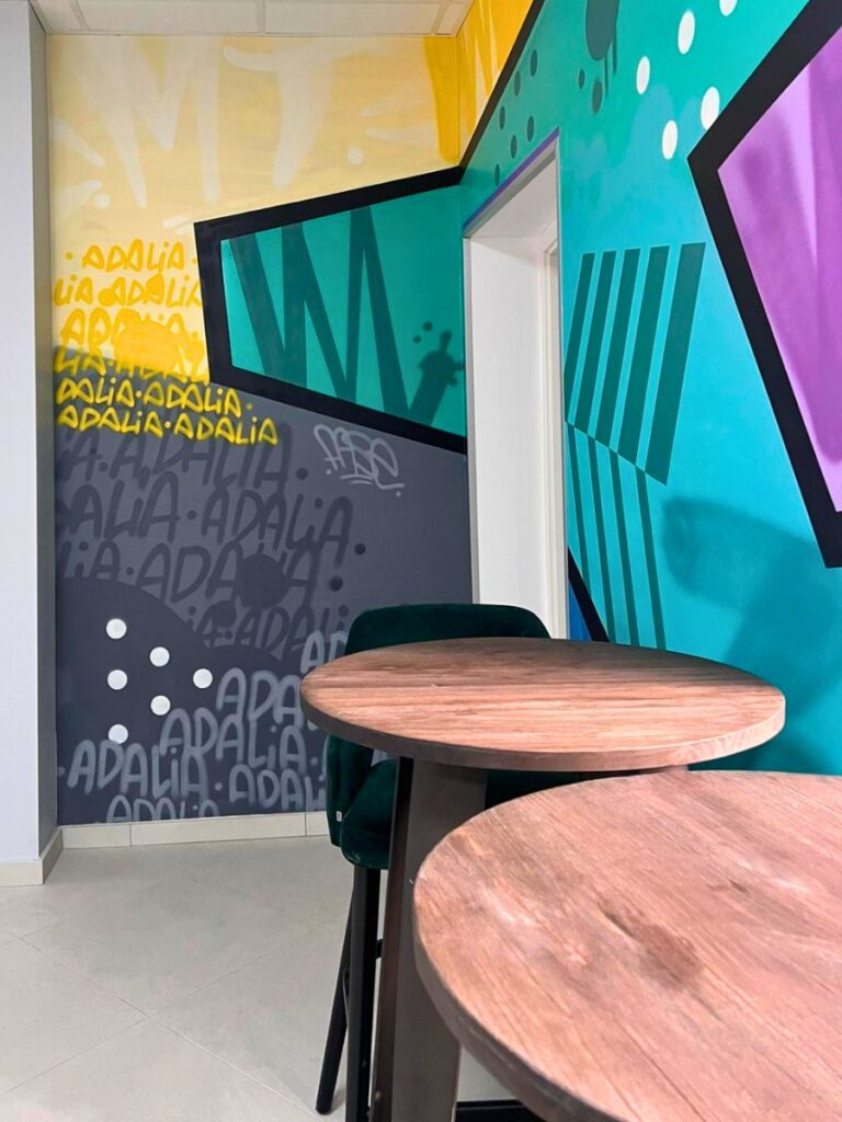 Espace détente de l'école Adalia avec tables rondes et fresque murale colorée