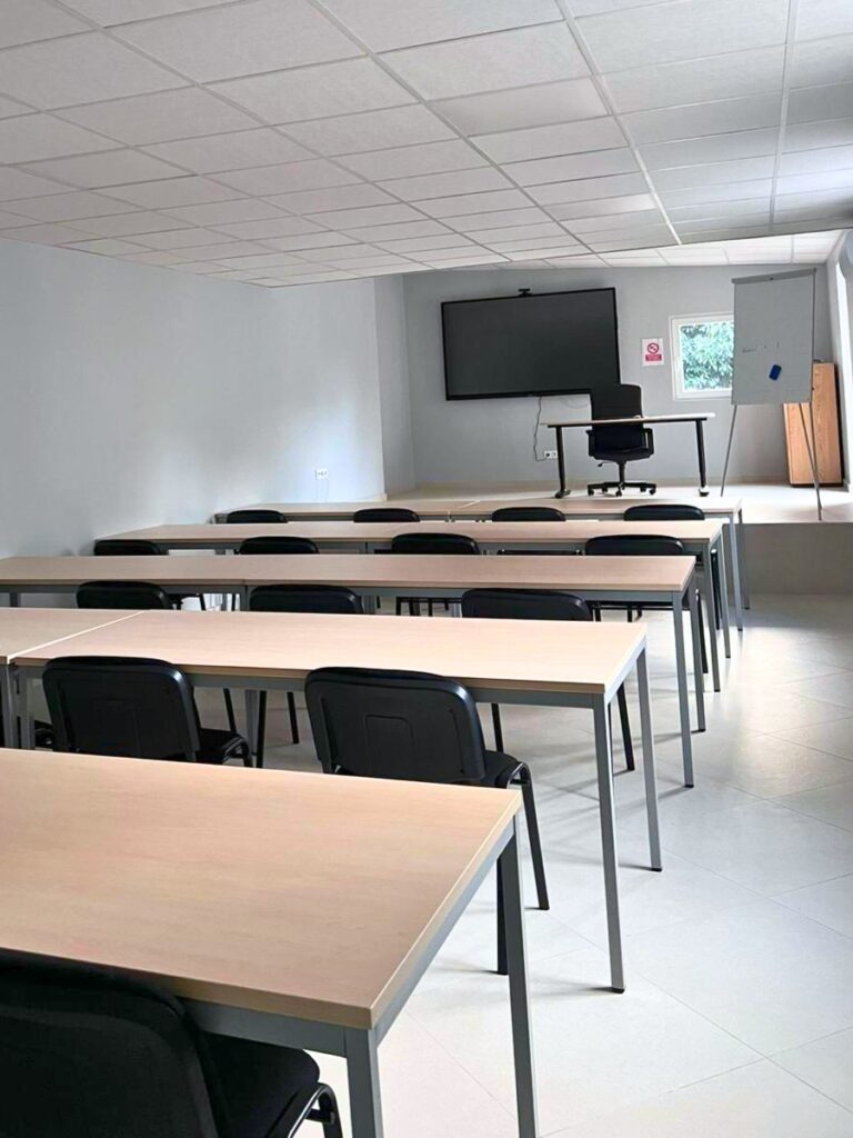 Grande salle de classe avec tables espacées et écran mural